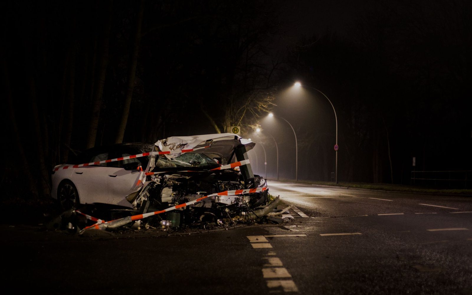 A damaged car sits on a dimly lit street at night after a collision.