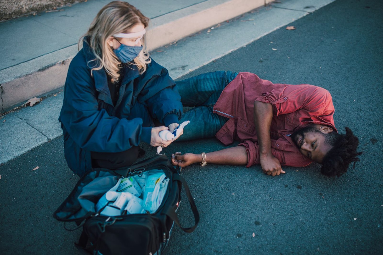 A paramedic kneels beside an injured man lying on the roadside, giving first aid.