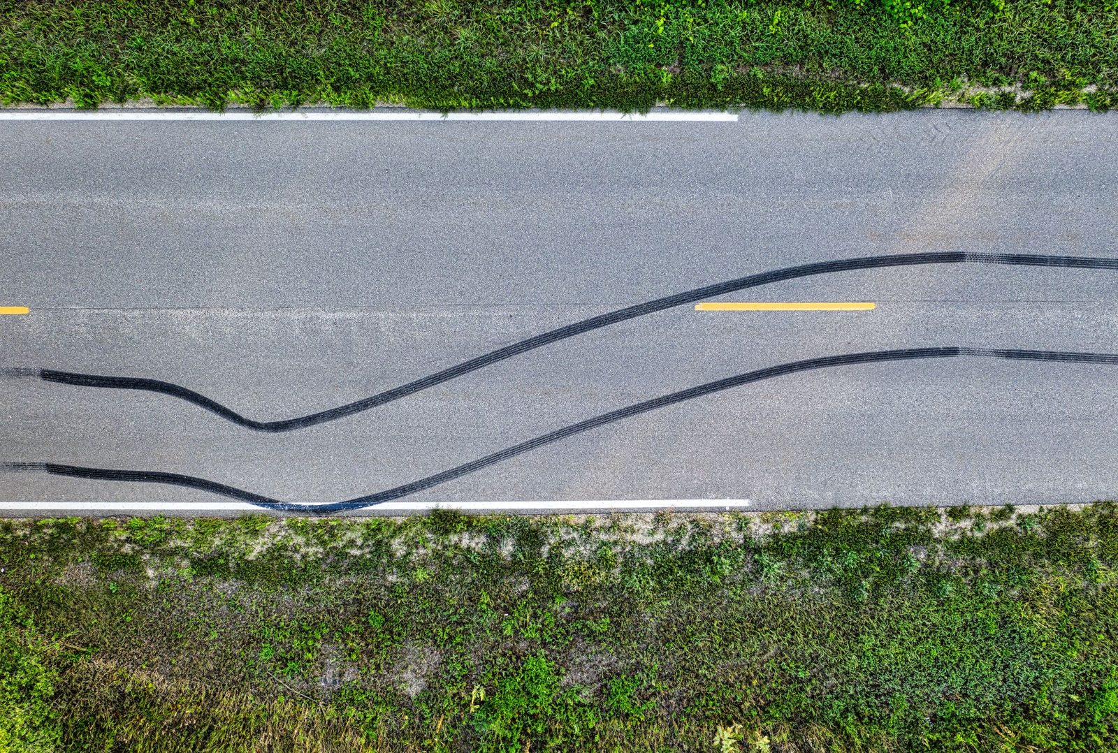 Aerial drone view of tire skid marks curving across a rural road.
