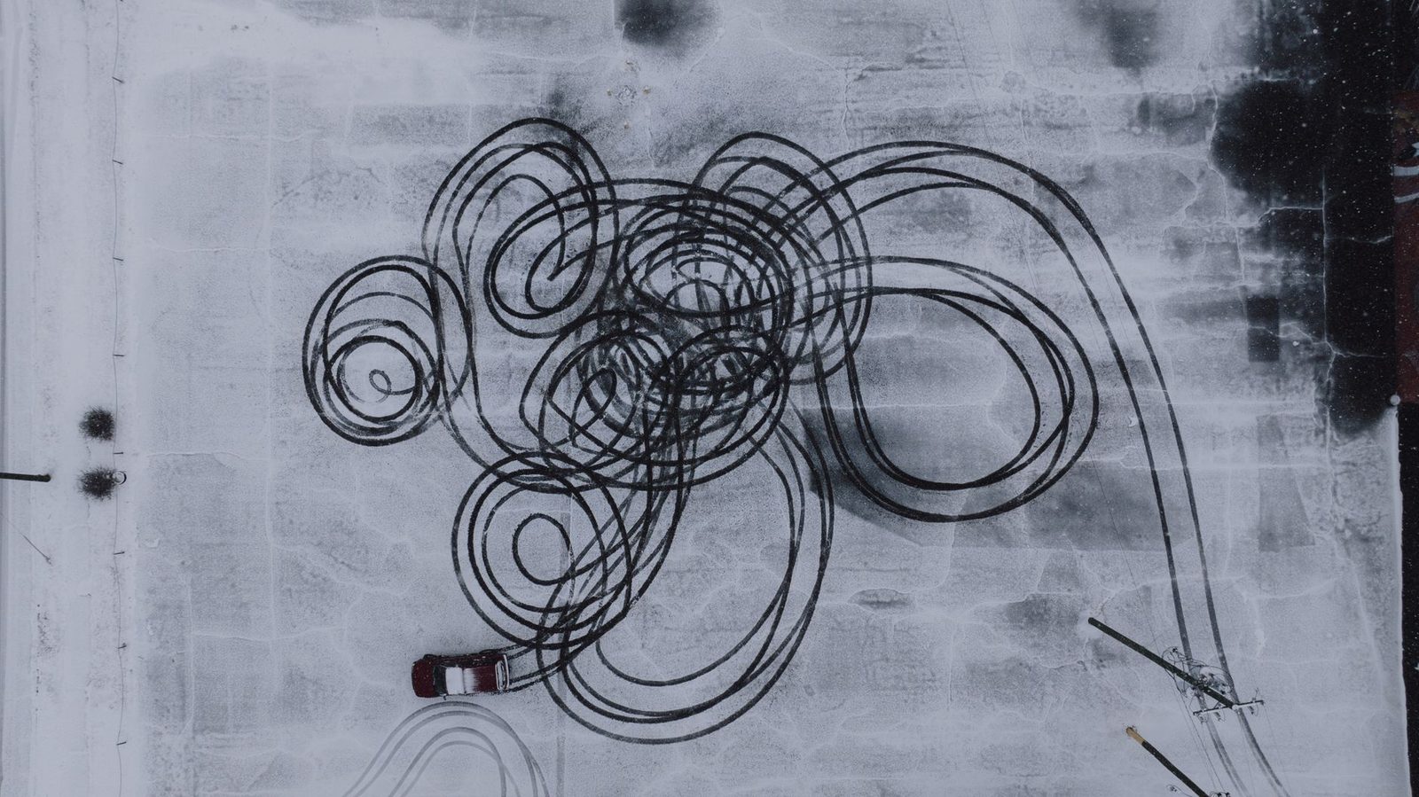 Aerial view of tire tracks curving across a snowy road, showing winter driving patterns.