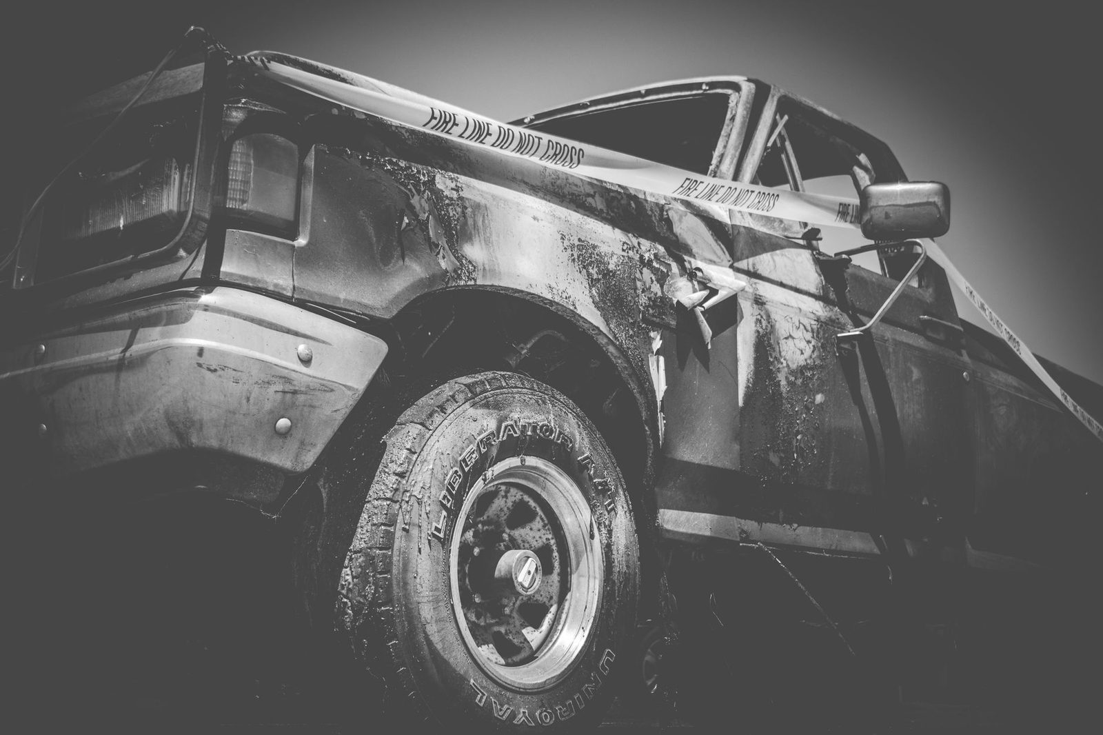Black-and-white photo of a damaged truck behind police tape at an accident scene.