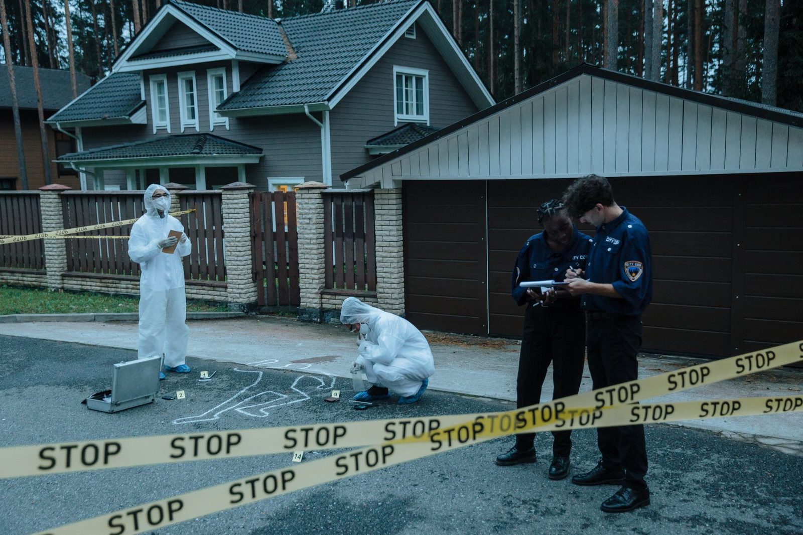 Forensic investigators and police officers process a suburban crime scene, placing evidence markers on the ground.