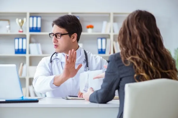 A doctor holding their hands up, in an effort to convey 'No" to a patient.
