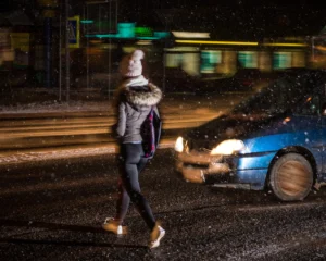 A person crossing the street at night while a car is coming.