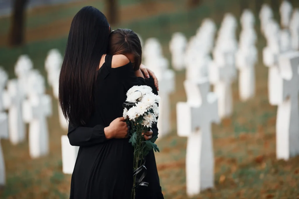 Two people, graveside, crying.